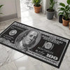 A black imitation hundred dollar bill is laid on a white tile floor next to potted plants.