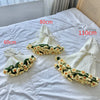 Hand knitted white blanket with floral rose accents displayed on a white bed sheet.