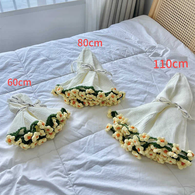 Hand knitted white blanket with floral rose accents displayed on a white bed sheet.
