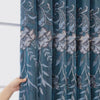 A close-up of a teal dual-layer curtain featuring embroidered floral and leaf patterns.