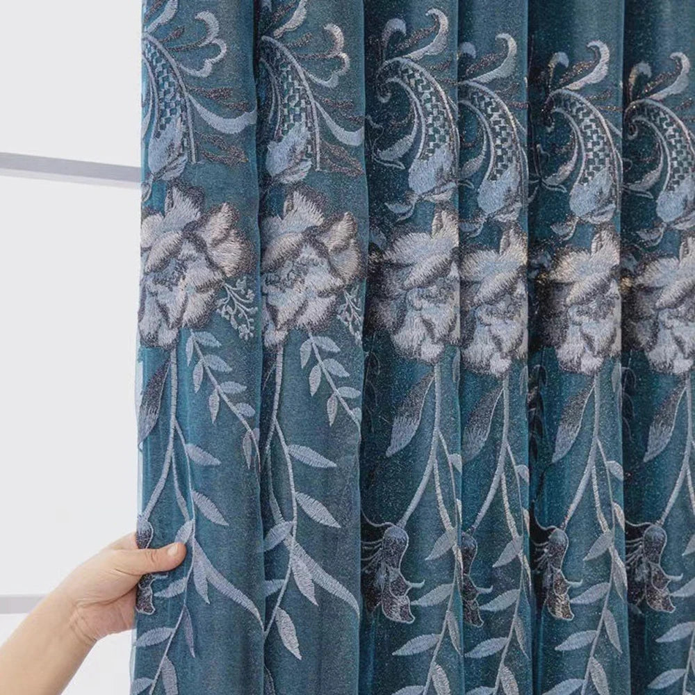 A close-up of a teal dual-layer curtain featuring embroidered floral and leaf patterns.