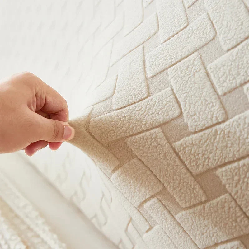 A hand touches a beige plush quilted fabric with a woven pattern on a wall surface.