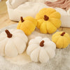 A collection of plush pumpkin-shaped throw pillows in yellow and cream colors resting on a light fabric.