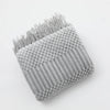 A gray knitted tassel throw blanket with a textured surface and frayed edges.