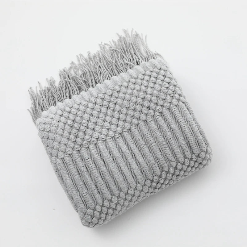 A gray knitted tassel throw blanket with a textured surface and frayed edges.