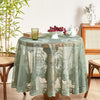 A round floral lace tablecloth in sage green with a tatting weave displayed on a wooden pedestal.