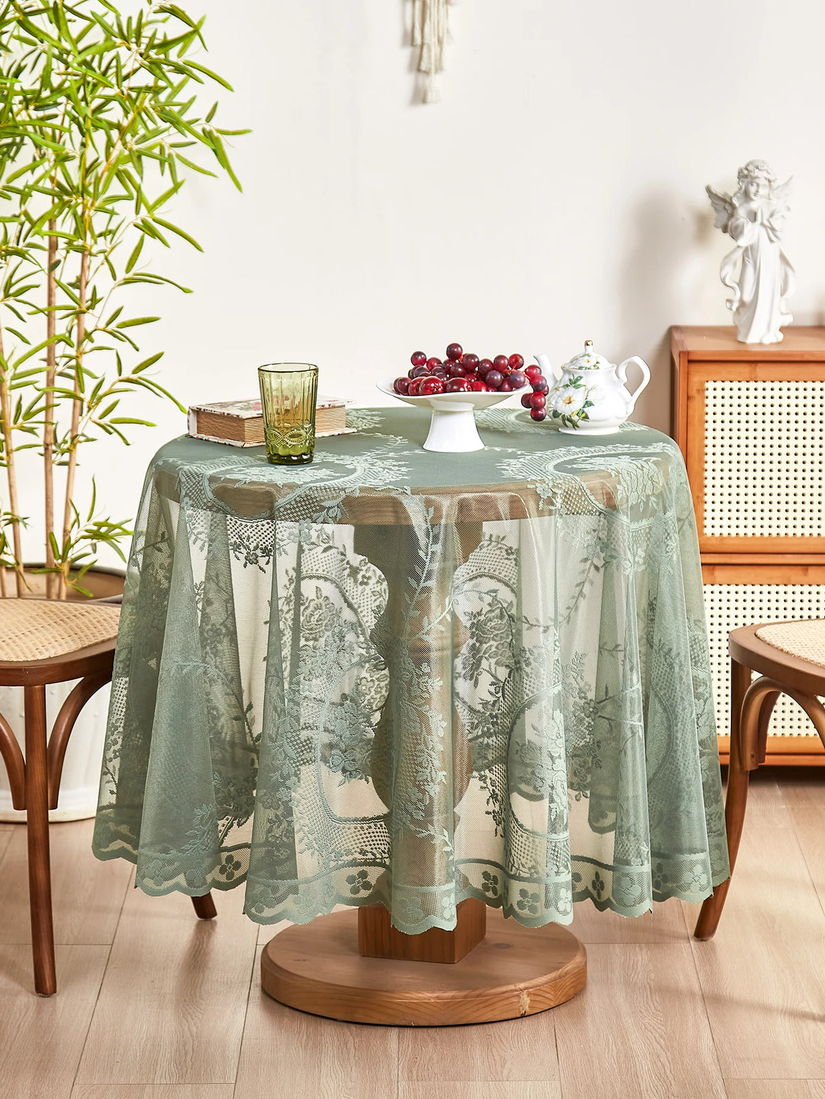 A round floral lace tablecloth in sage green with a tatting weave displayed on a wooden pedestal.