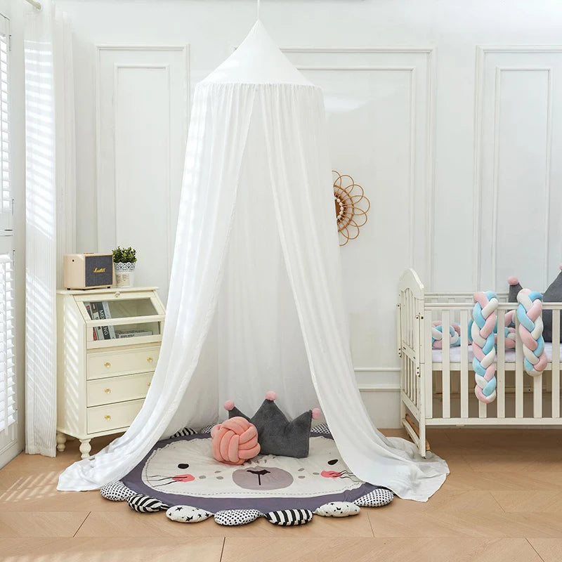 A white princess hanging bed canopy with sheer fabric draped over a wooden crib and decorated with soft toys.