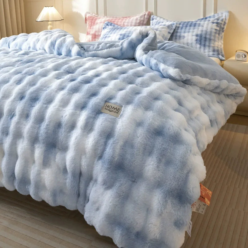 A light blue plush rabbit quilt comforter with white piping and patterned pillows on a bed.
