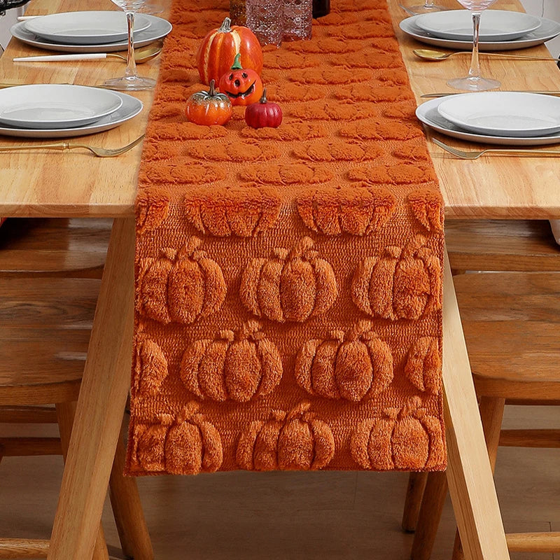 An orange felt table runner decorated with embossed pumpkin patterns on a wooden dining table.