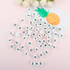 White alphabet beads scattered on a pink background next to a pineapple and white flowers