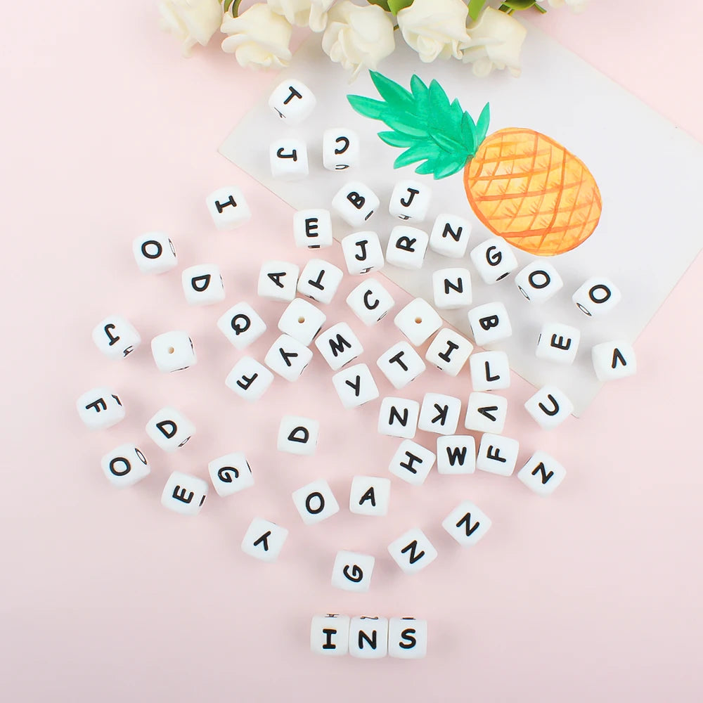White alphabet beads scattered on a pink background next to a pineapple and white flowers