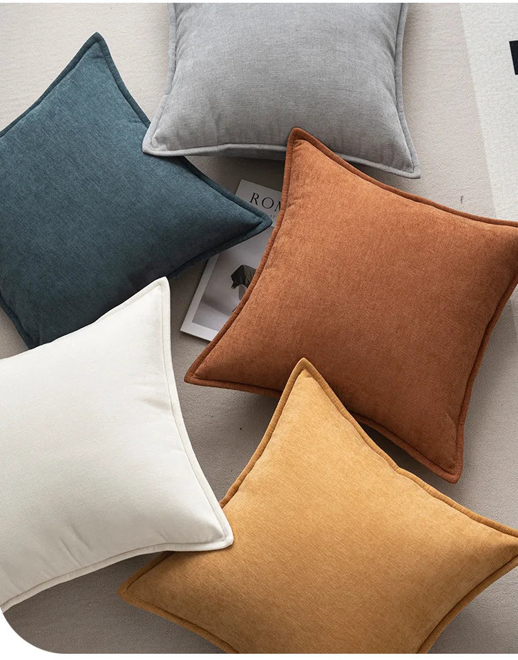 A collection of soft chenille throw pillows in shades of teal, gray, rust, and mustard on a neutral background.