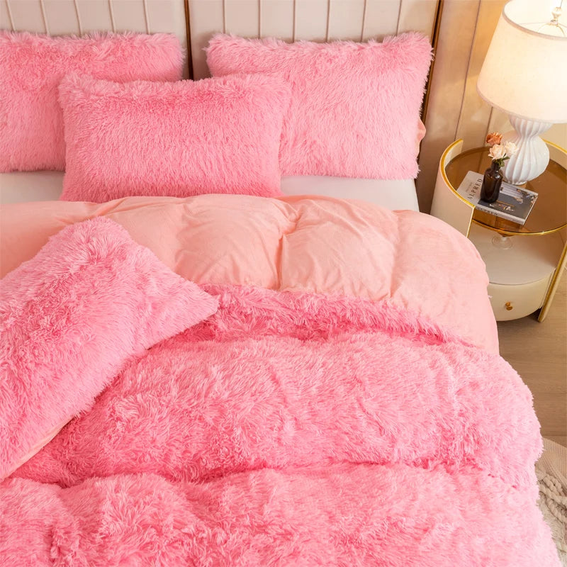 A set of pink fluffy pillows and a pink plush duvet cover on a bed.