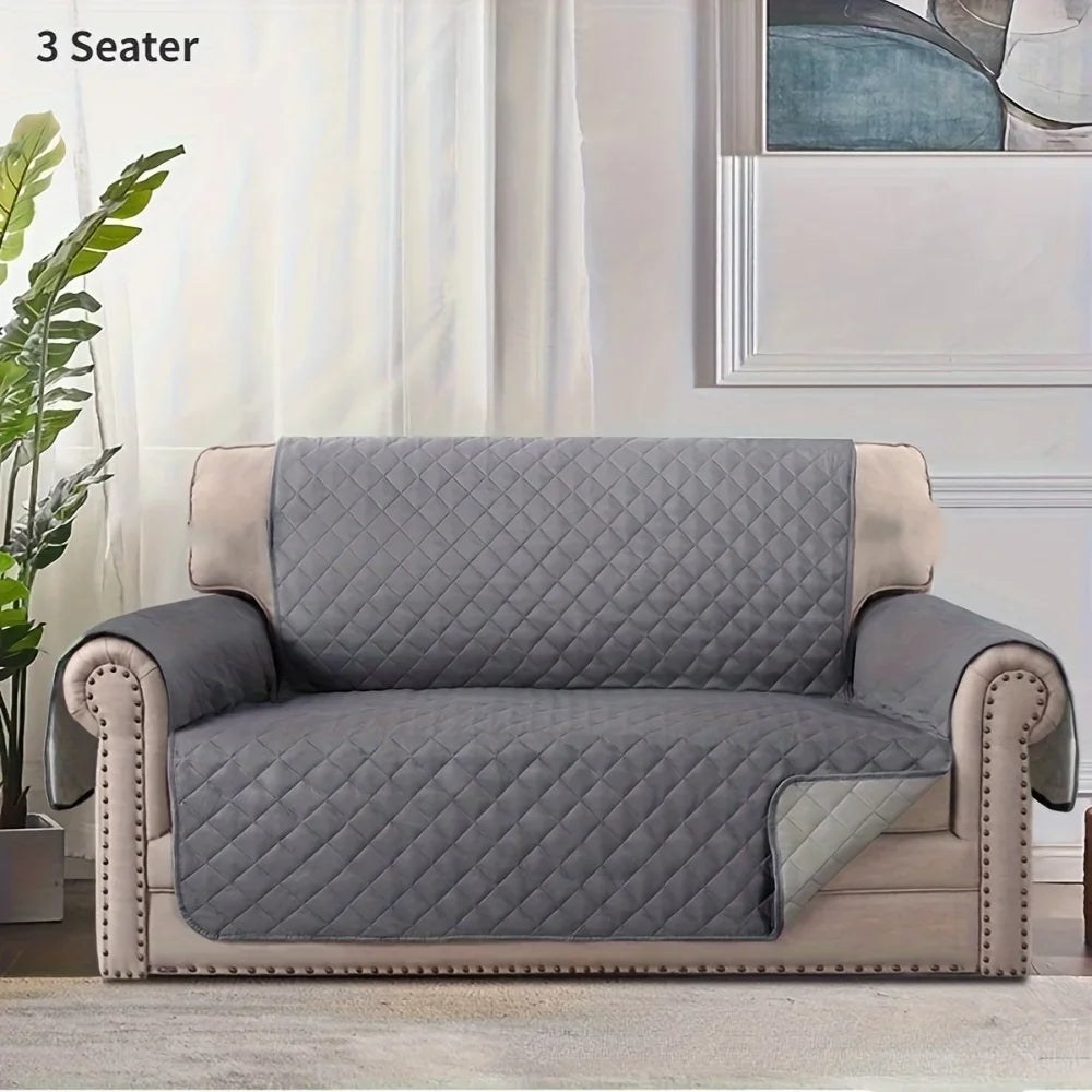 A gray slip-on protective sofa cover for a 3 seater armchair with beige trim and quilted texture.