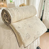 A rolled cream-colored quilt blanket with a pastoral print featuring small animal figures is displayed on a white surface.