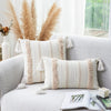 A beige tufted throw pillow cover with fringed tassels resting on a light gray sofa.