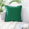 A deep emerald green velvet decorative cushion cover resting on a white knitted blanket.