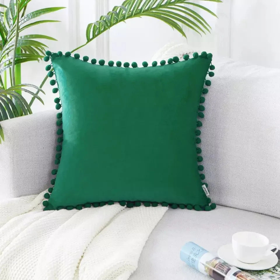 A deep emerald green velvet decorative cushion cover resting on a white knitted blanket.