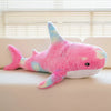 A pink and blue giant shark plush toy lying on a light-colored surface.