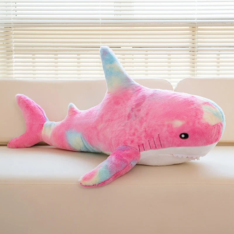 A pink and blue giant shark plush toy lying on a light-colored surface.