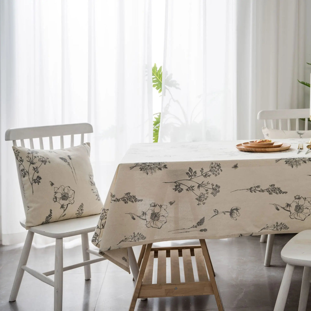 A linen tablecloth with a botanical print is displayed on a white wooden table in a bright room.