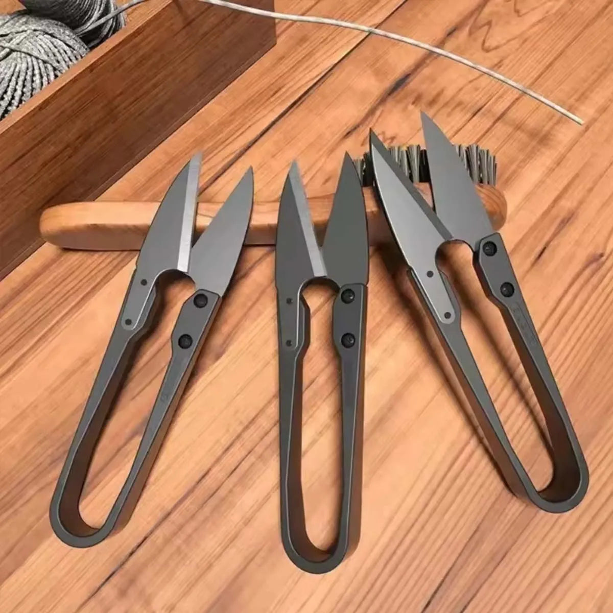 A pair of ergonomic stainless steel thread snip scissors resting on a wooden surface.