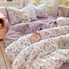 A set of lavender and white floral patterned microfiber duvet covers and pillowcases displayed on a bed.