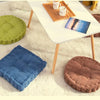 A set of three tufted corduroy floor seat cushions in shades of green, blue, and brown resting on a white table.