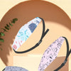 A pink and blue patterned baby head and neck support pillow is shown resting on a light brown surface.