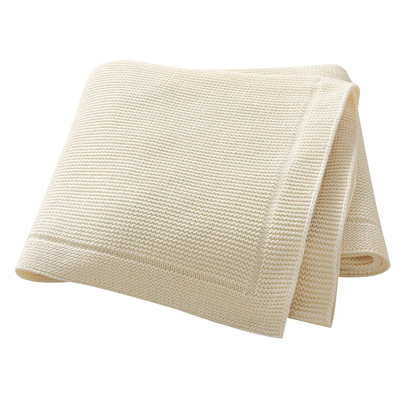 A folded cream colored all-season cotton baby swaddle blanket.