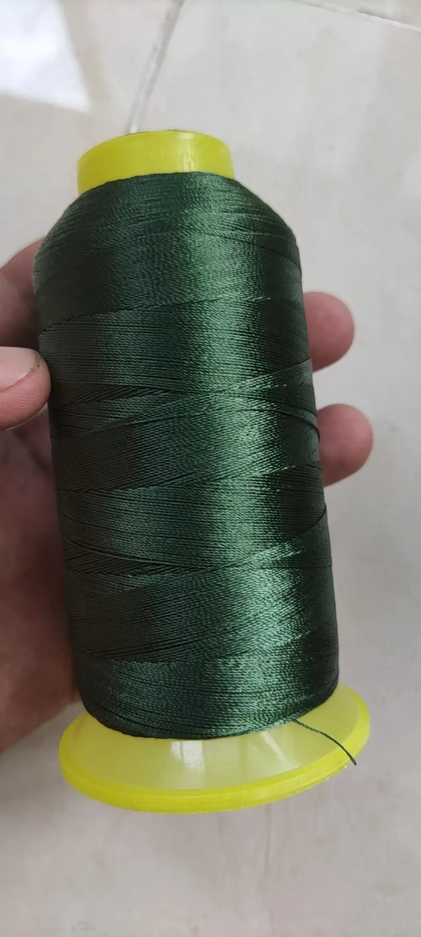 A spool of dark green high tenacity polyester sewing thread with a yellow plastic core.