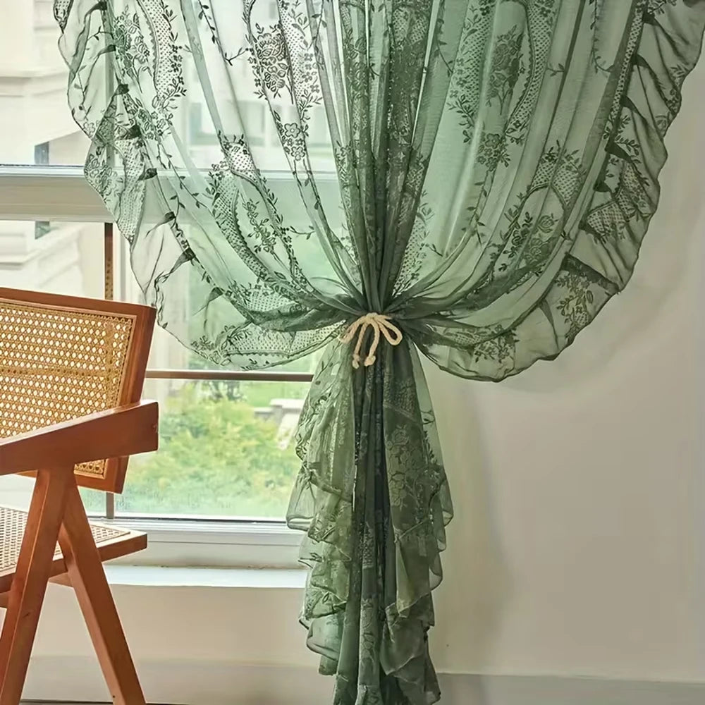 A sheer green lace floral window curtain is draped and tied in a window frame.