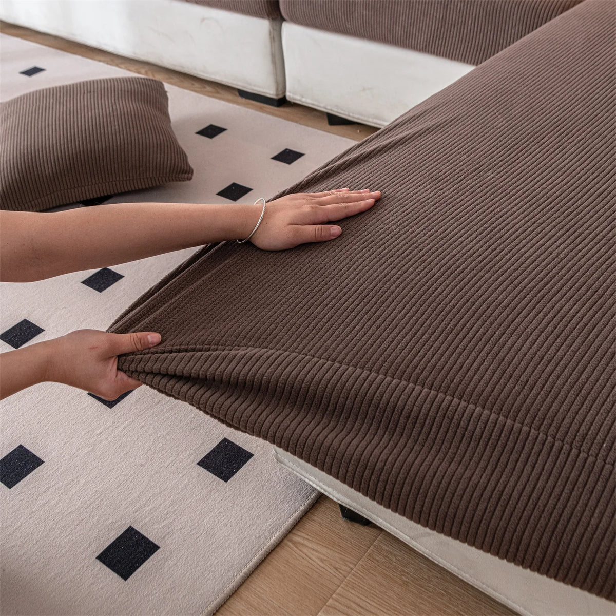 A hand is touching a brown removable jacquard seat cushion cover on a light-colored floor.