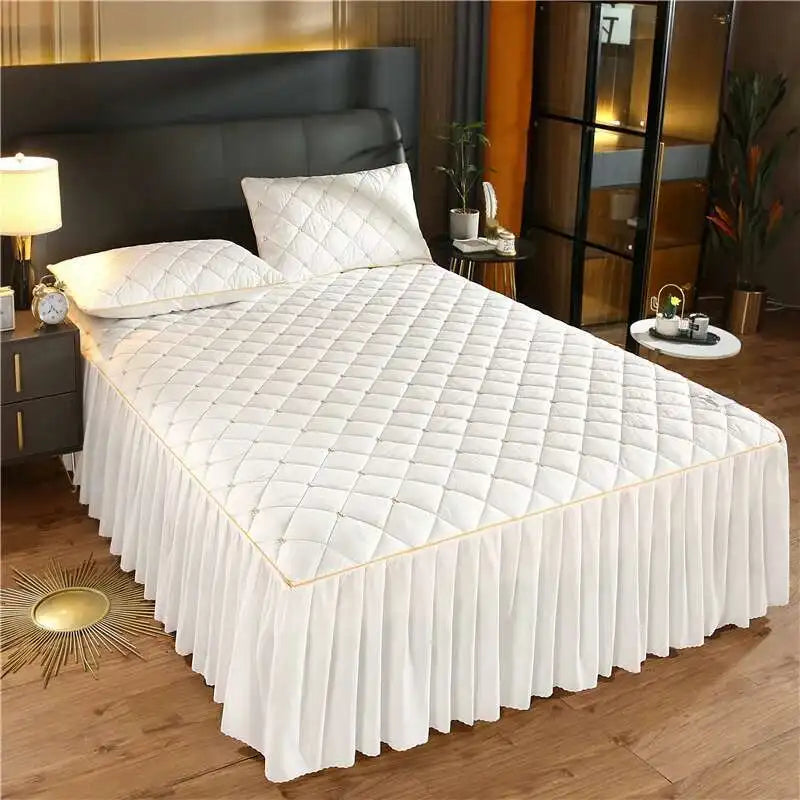 White quilted bed skirt with a gold trim covering a queen mattress.