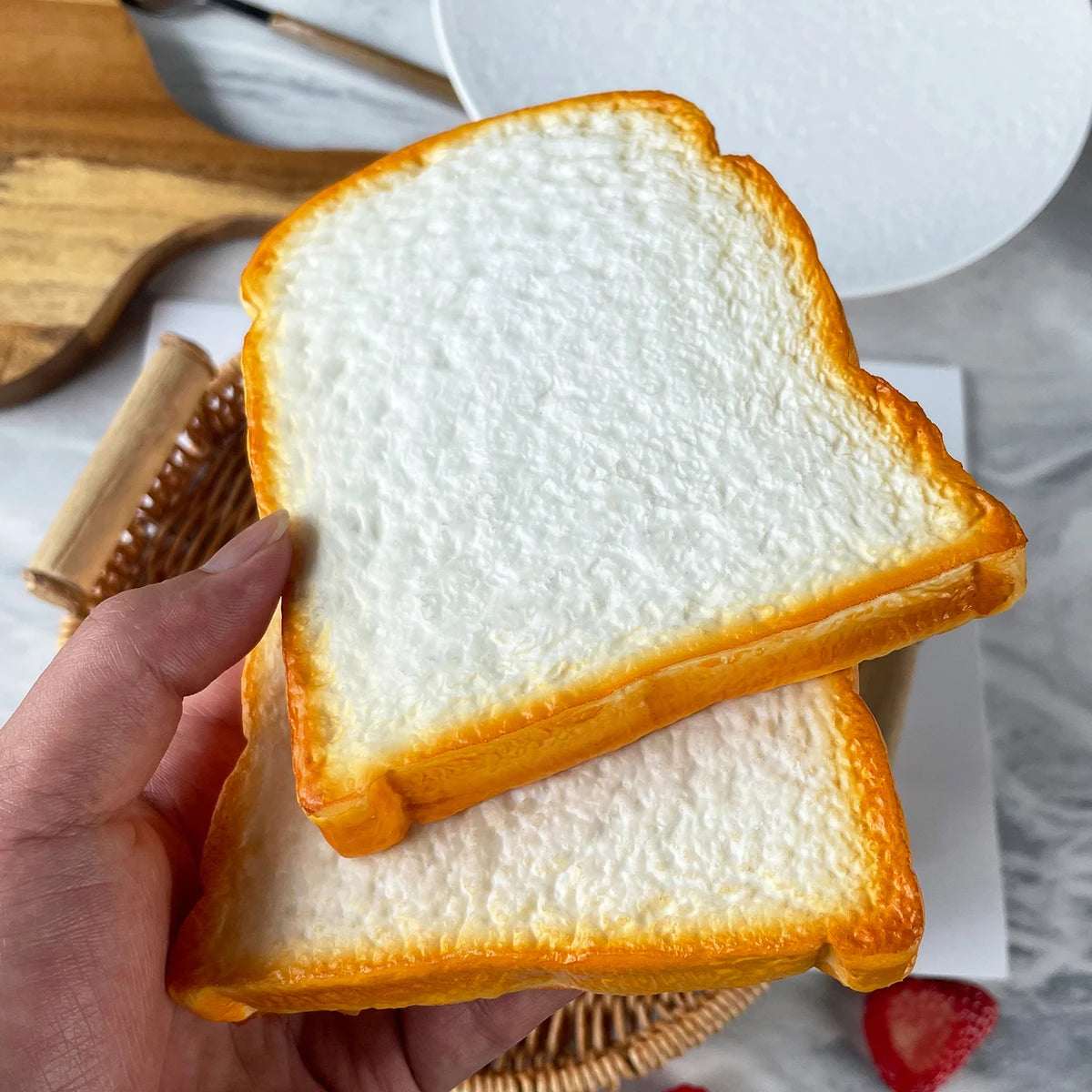 A hand holds two slices of golden brown toast on a white plate with a strawberry.