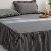 A black and white plaid cotton bed skirt cover draped over a bed, with pillows and wooden accessories nearby.