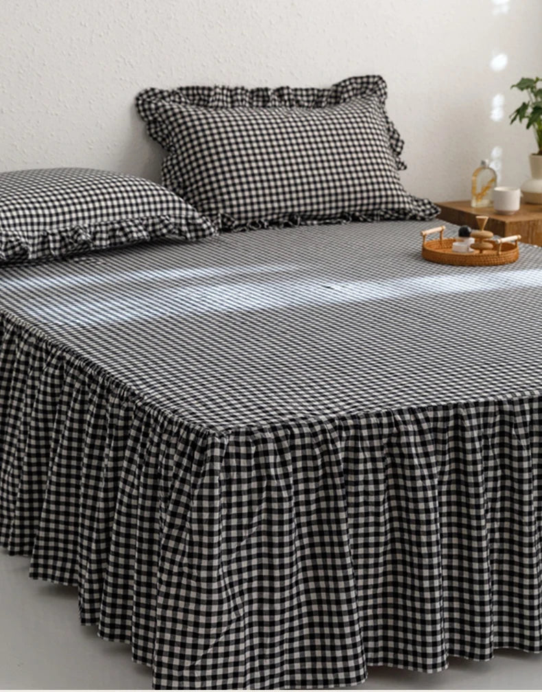 A black and white plaid cotton bed skirt cover draped over a bed, with pillows and wooden accessories nearby.