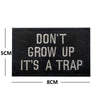 Black embroidered patch with white text that reads DON'T GROW UP IT'S A TRAP