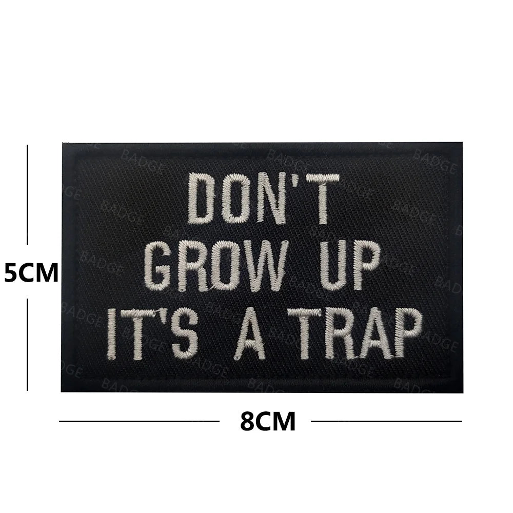Black embroidered patch with white text that reads DON'T GROW UP IT'S A TRAP