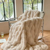 A fluffy beige faux fur throw blanket draped over a metal chair near a window.