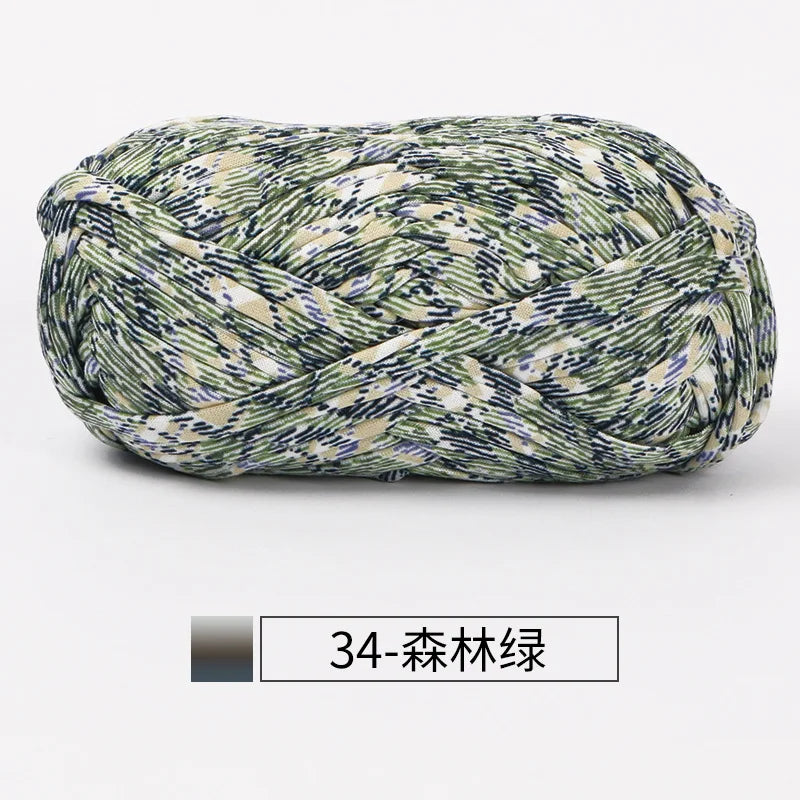 A ball of hand-dyed fabric strip yarn featuring a mottled green and beige pattern.