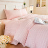 A pink seersucker duvet cover and pillow set displayed on a bed with light wood furniture.