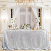 A silver sequin rectangle table cover draped on a table, decorated with white flowers and gold accents.