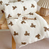 A white muslin blanket with brown bear print is rolled up and laid out on a wooden surface.