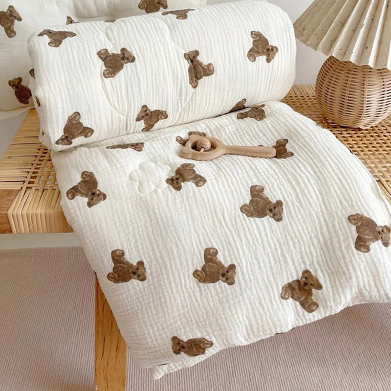 A white muslin blanket with brown bear print is rolled up and laid out on a wooden surface.