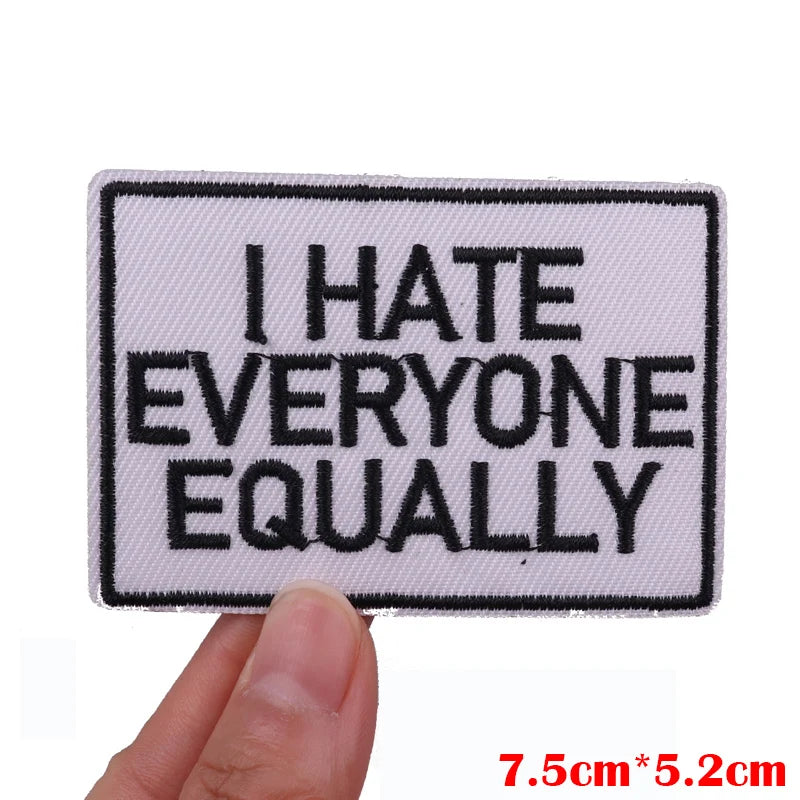 A white embroidered patch with black text that reads I HATE EVERYONE EQUALLY
