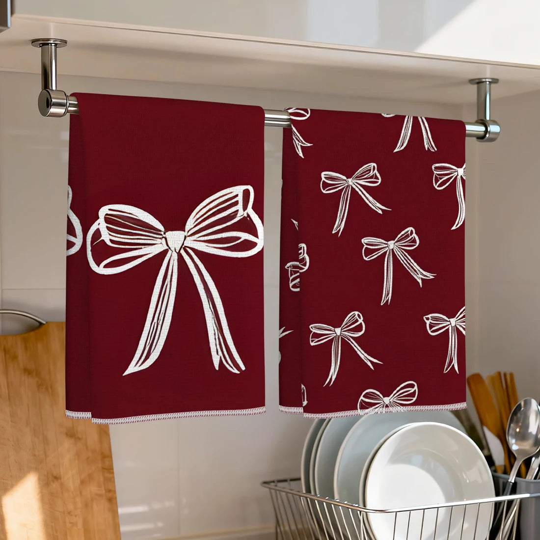 Two maroon kitchen towels with white bow patterns hanging on a metal rack.