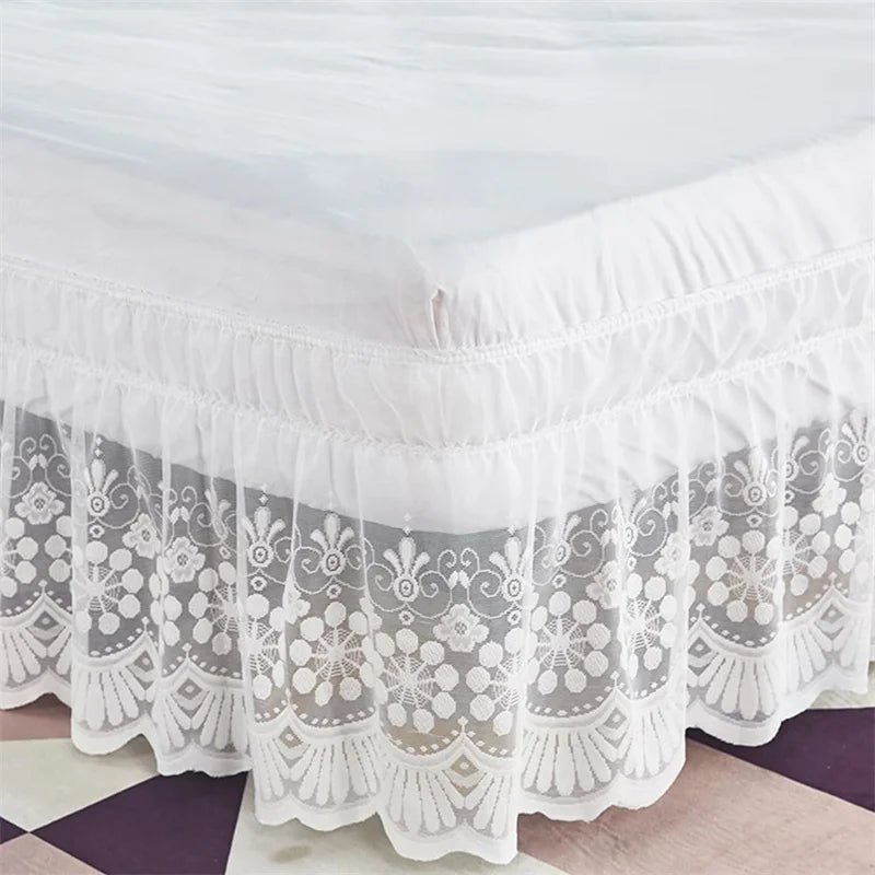 White lace ruffle bed skirt with elastic trim displayed on a bed.