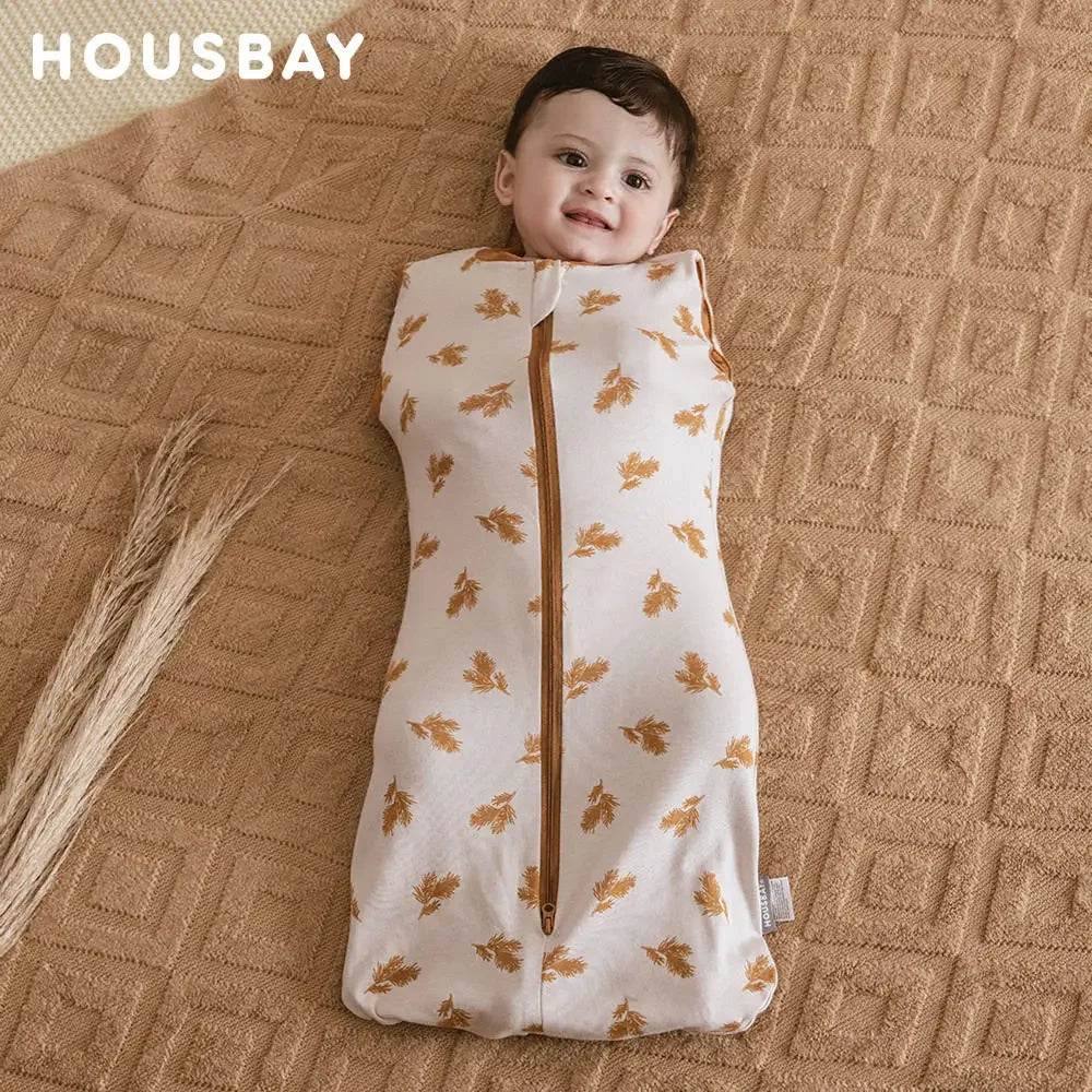 A baby wearing a beige soft cotton sleeping bag or swaddle with a subtle floral pattern, lying on a woven fabric background.